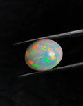 Oval opal cabochon with bright green fire and red-orange sparks between tweezers