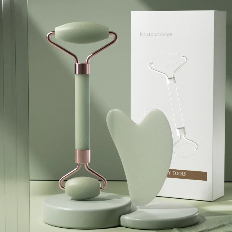 Sage green dual-ended facial roller and heart-shaped gua sha board with rose gold metal accents, next to a white box.