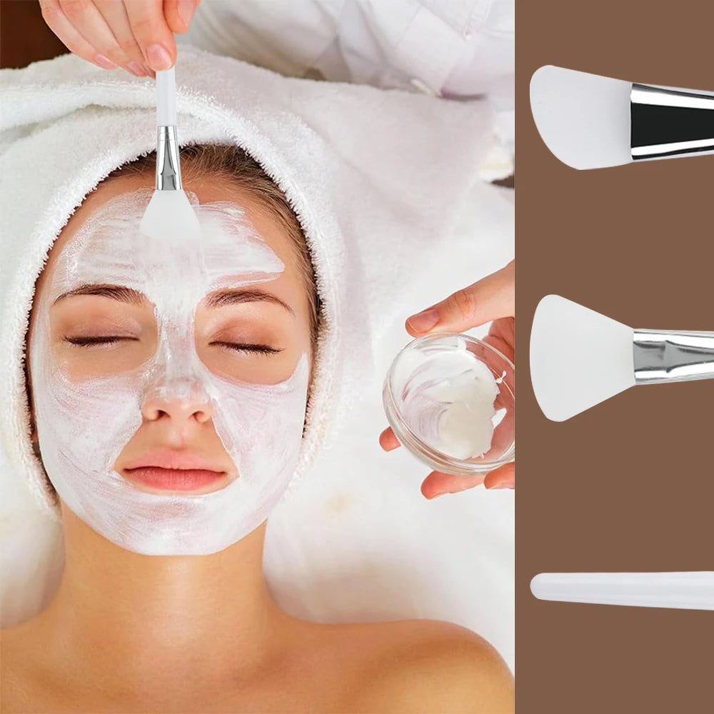 A person applies a white face mask using a soft white silicone spatula brush with a silver handle.
