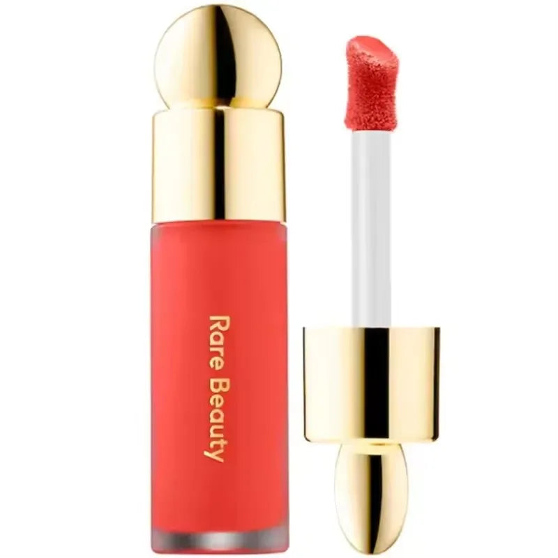 Rare Beauty matte lipstick in vibrant coral with a smooth, moisturizing finish and luxurious gold applicator cap.