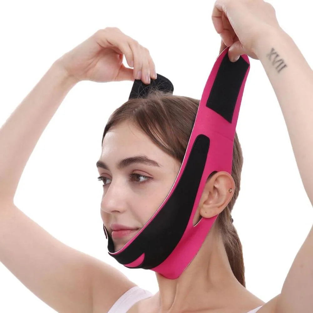 A woman wearing a bright pink and black elastic V-line face slimming bandage strap secured around her chin and head.