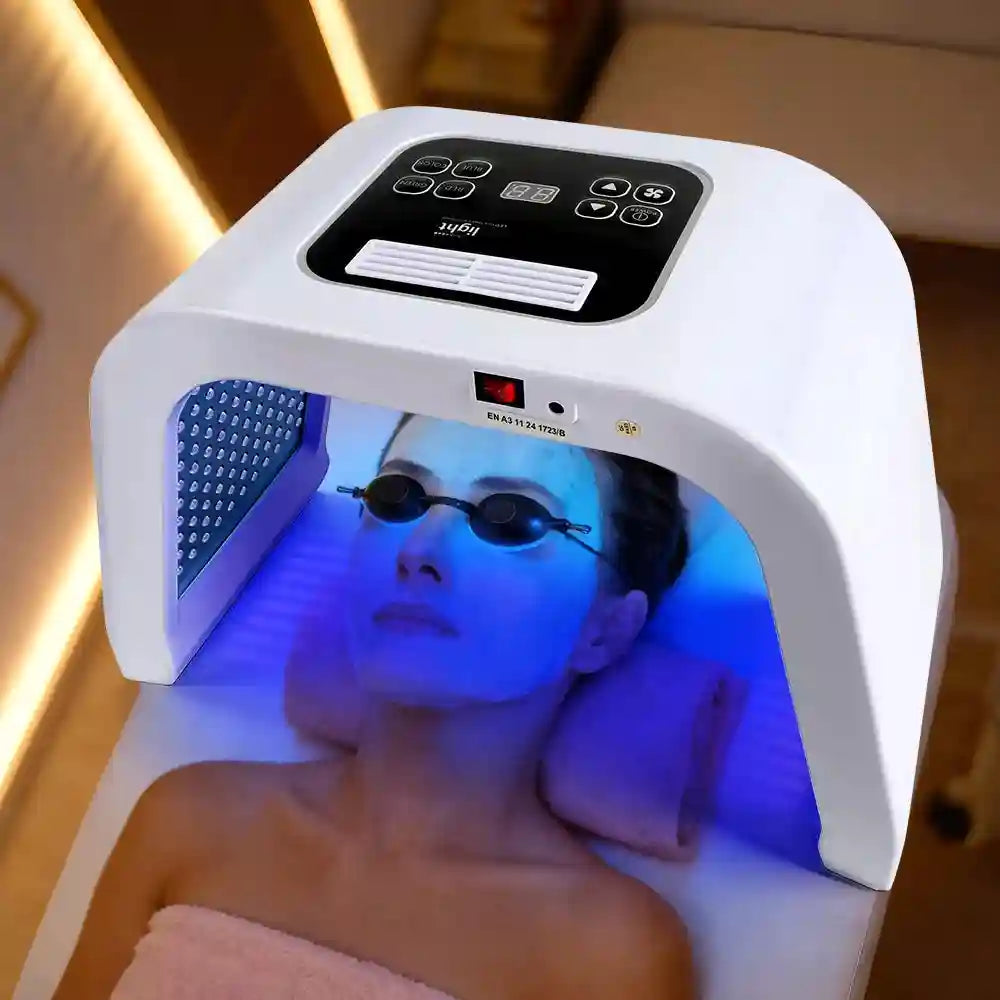 White LED facial therapy machine with blue light illuminating a person wearing protective eyewear while lying down.