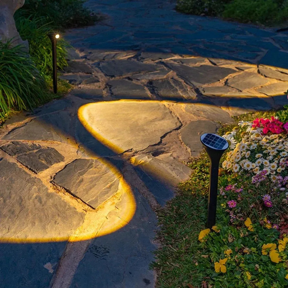 Two black solar LED landscape spotlights illuminate a stone garden pathway at night.