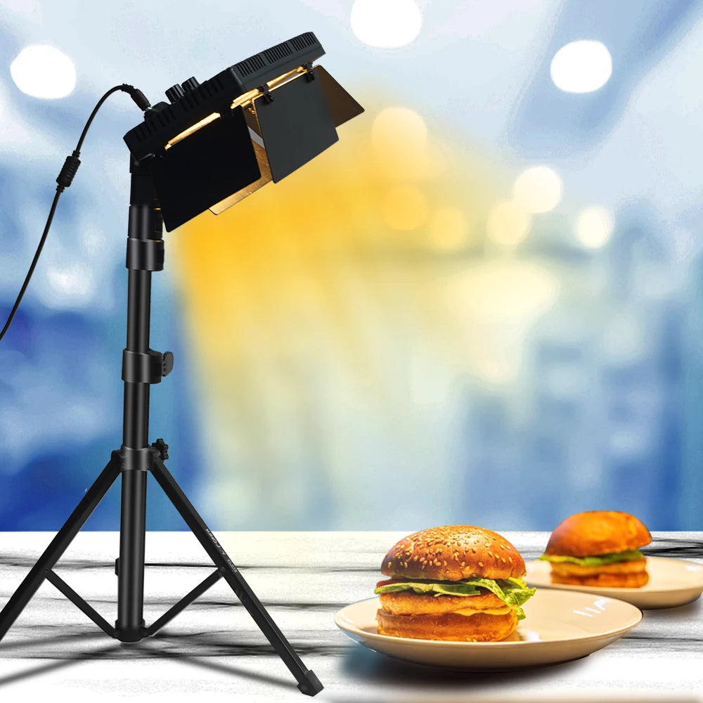 Black LED video light with adjustable metal barn doors on a tall tripod stand, illuminating plates of burgers.