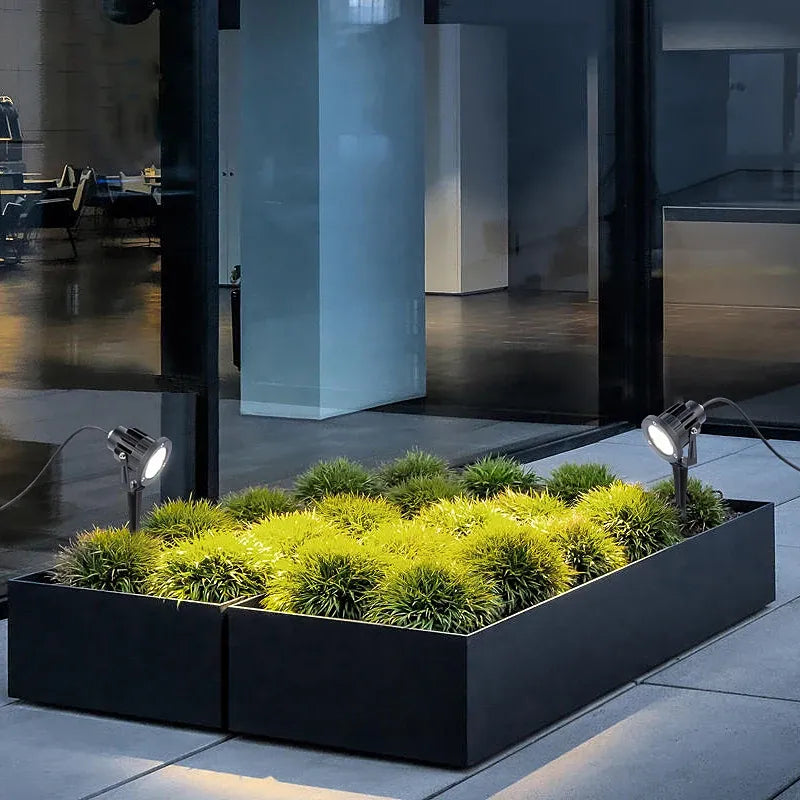 Two outdoor LED landscape spike spot lights with black round heads in a garden bed