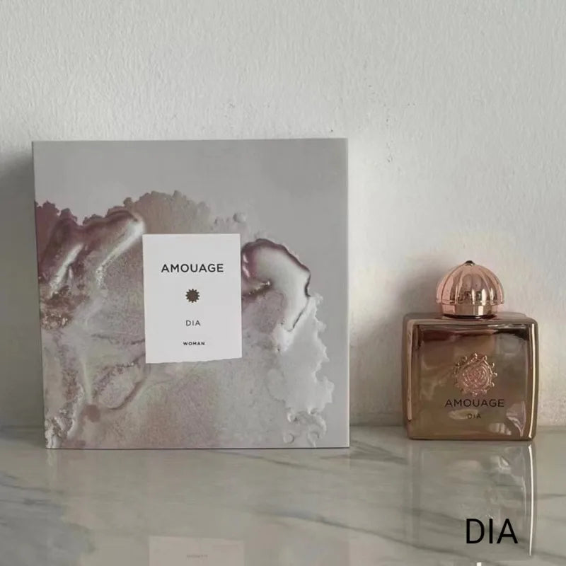 Amouage Dia Woman perfume in a metallic gold rectangular bottle with a domed cap, next to its marbled gray gift box.