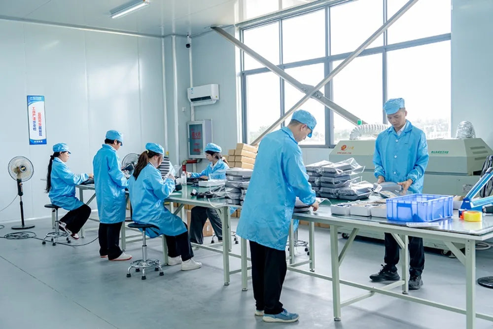Workers in blue uniforms assembling Frovab rTMS brain stimulation machines for Parkinson's rehab in a clean factory.