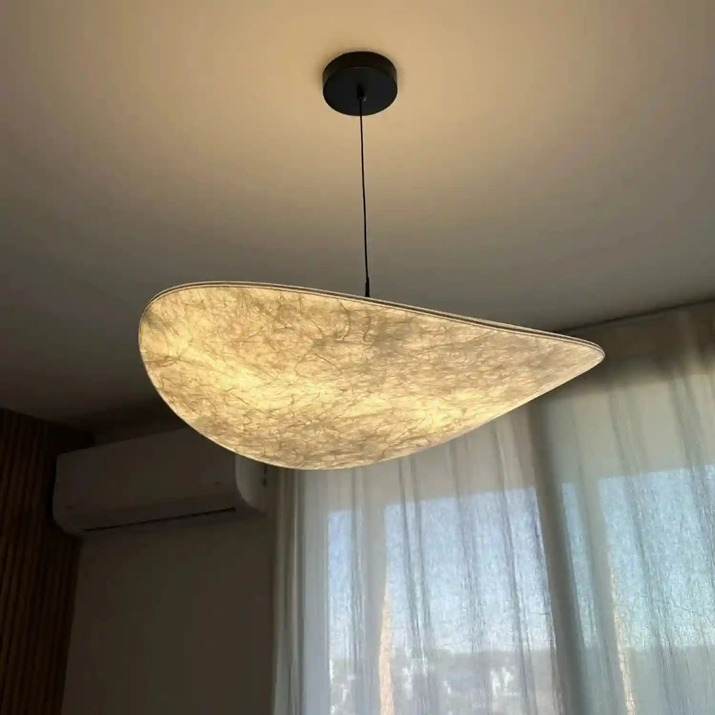 Large, curved pendant light with a textured, off-white paper shade and black ceiling mount for interior ambient