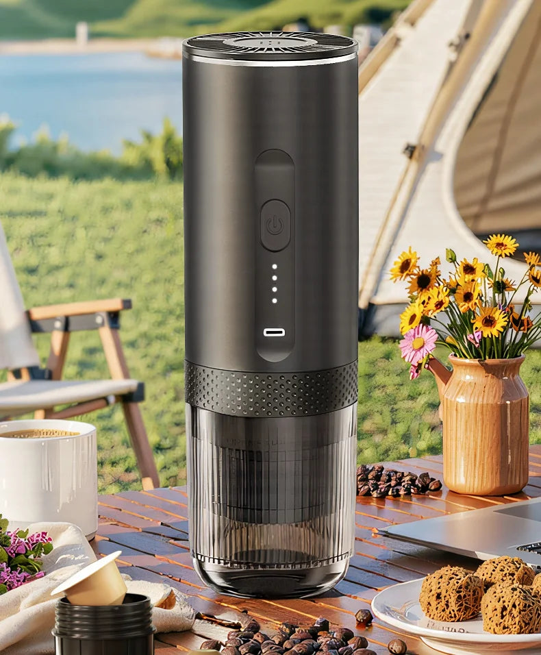 Portable black electric coffee maker with clear chamber for camping on a wooden outdoor table.