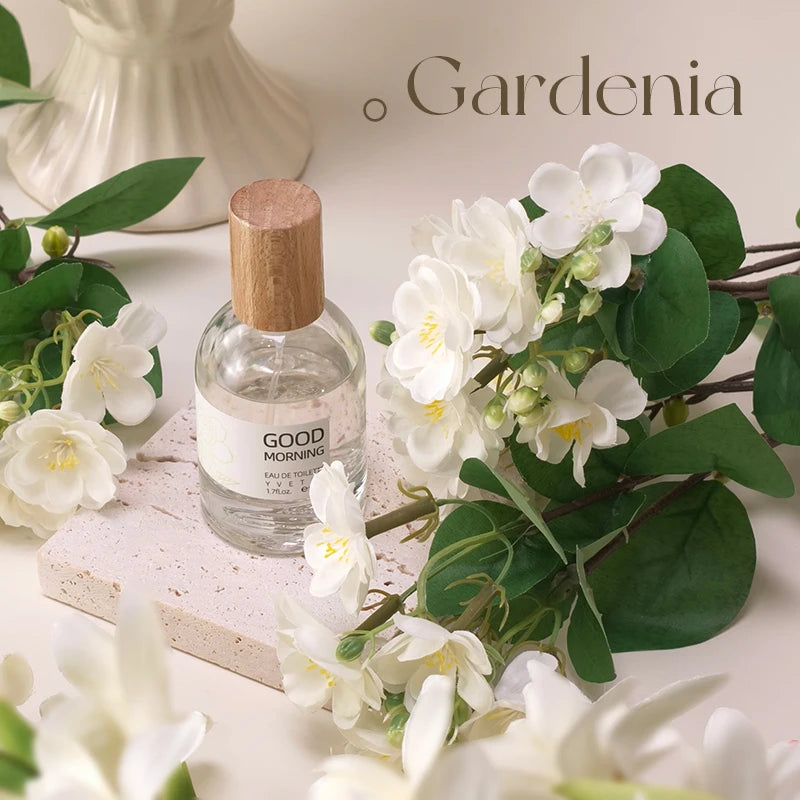 Elegant Gardenia perfume in a clear glass bottle with a wood cap, displayed on stone with fresh white flower stems.
