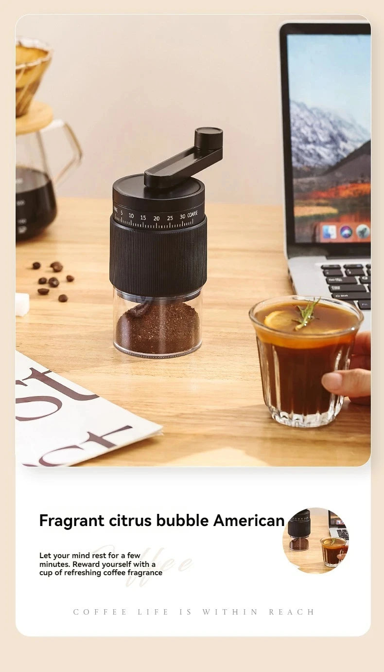Black manual coffee grinder with adjustable grind settings and transparent base on a desk with iced coffee.