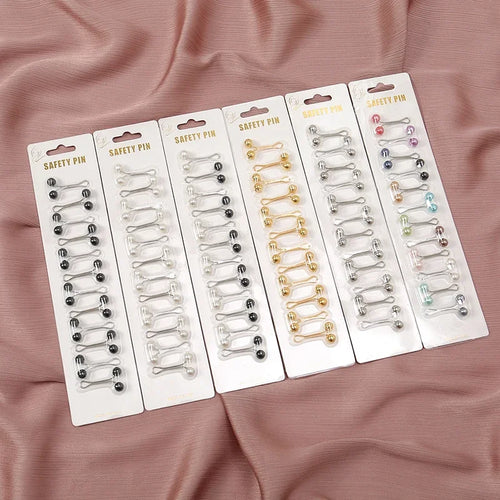 Six packs of 12 Tidesmit metal hijab safety pins with decorative colorful spherical beads on a mauve fabric background.