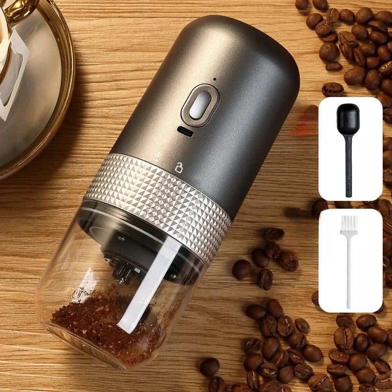 Portable charcoal grey electric coffee grinder with clear glass container, metal trim, coffee scoop, and brush.