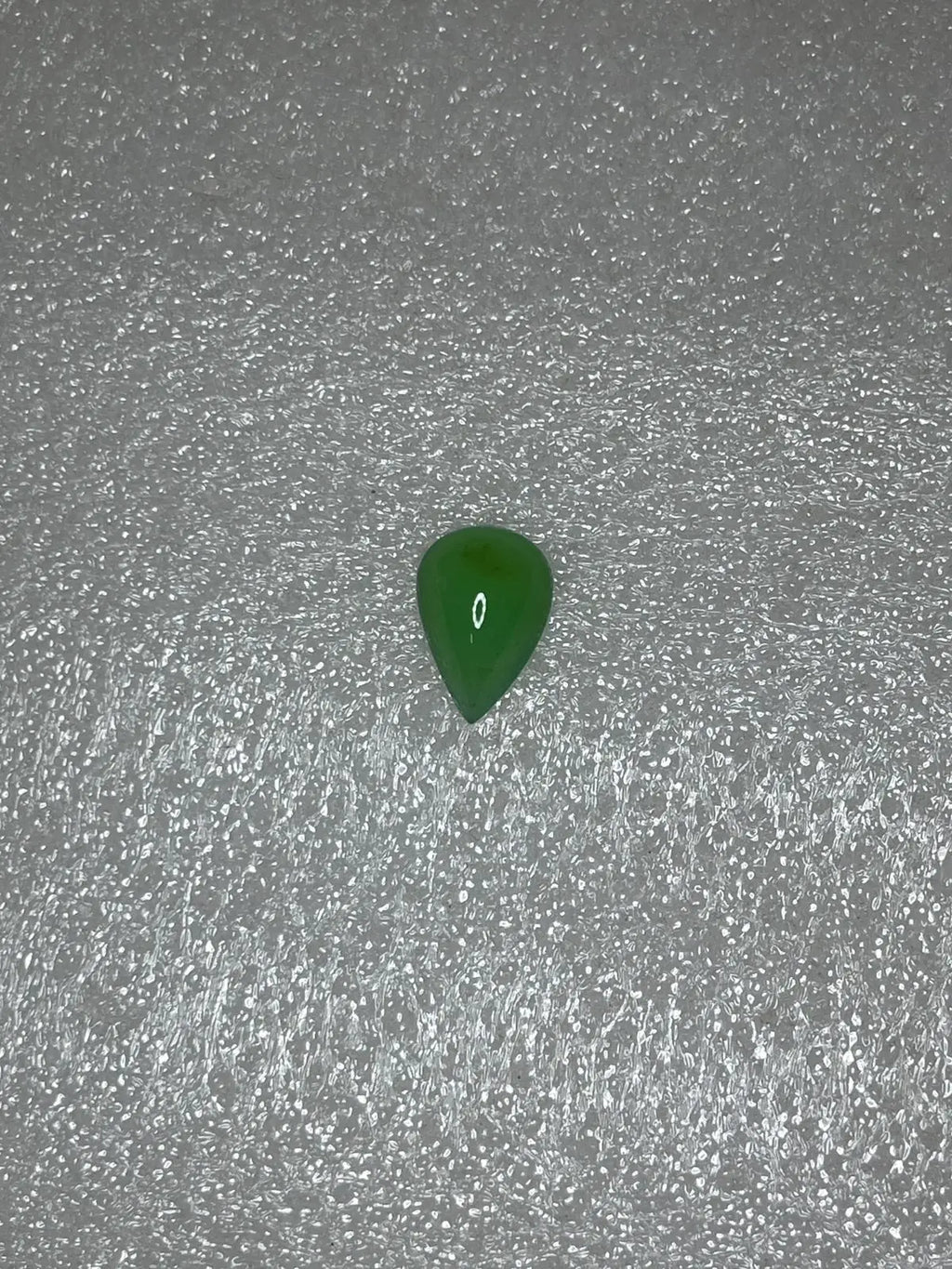 Dark green chrysoprase pear-shaped cabochon gemstone, polished teardrop on gray surface.