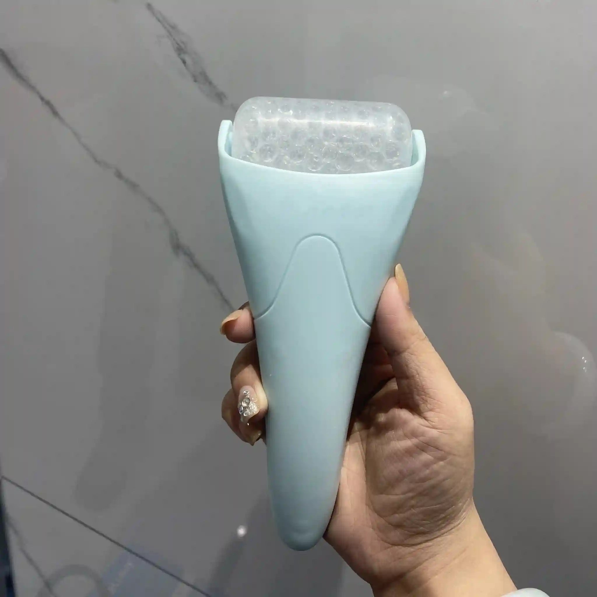 Handheld light blue facial ice roller with a textured, semi-transparent cylindrical cooling head.