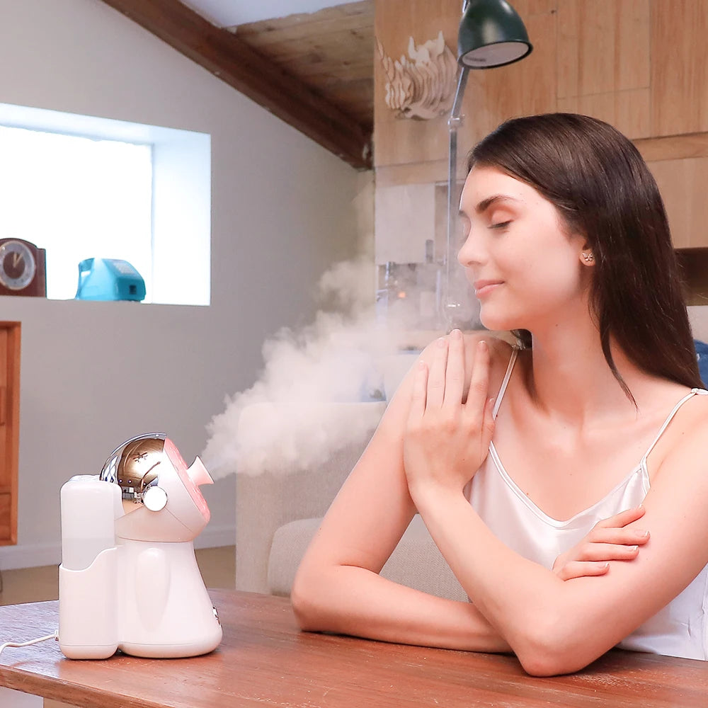 Small white and chrome desktop facial steamer emitting steam for skin hydration, set on a wooden table.