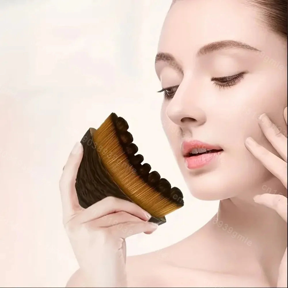 A person holding a curved, black-handled lymphatic face contouring brush with dense, tan-tipped synthetic bristles.