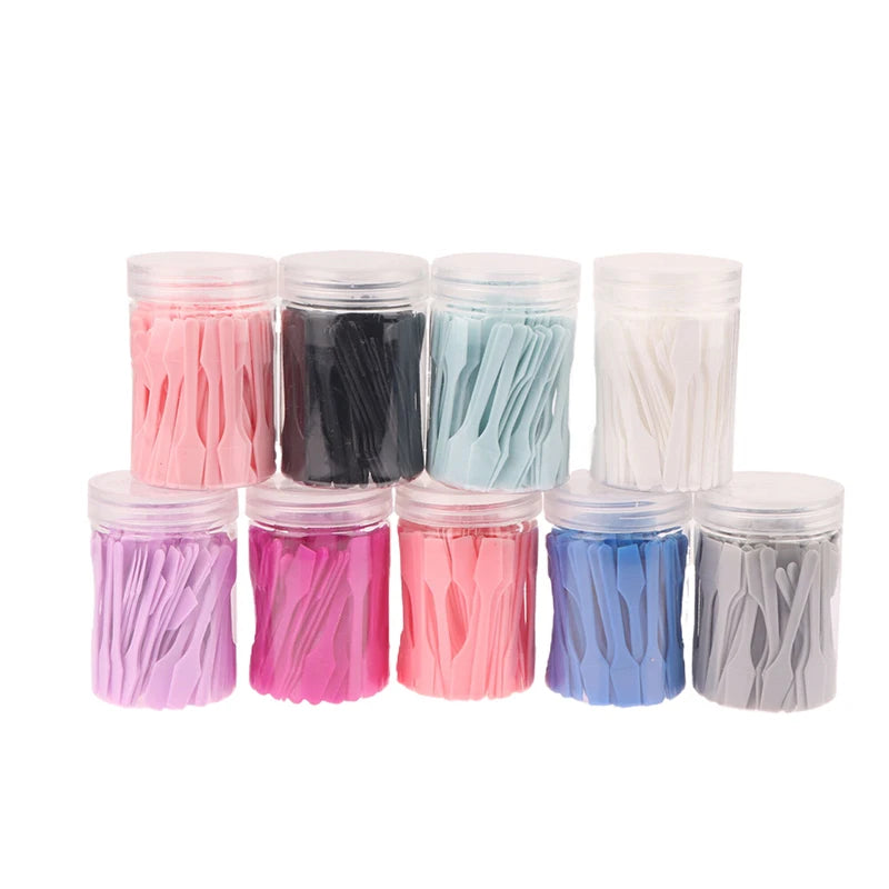 Nine clear plastic jars filled with small, colorful cosmetic spatulas in various shades, arranged on a white background.