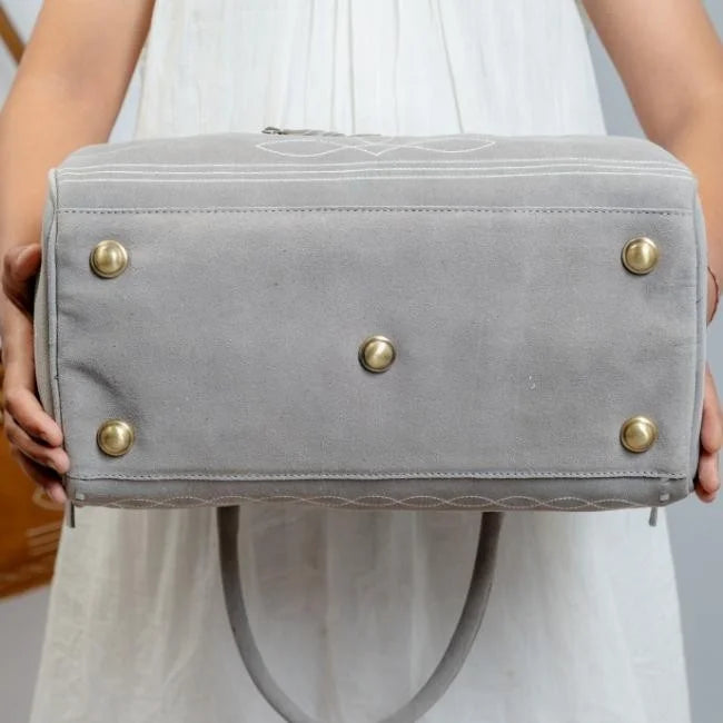 Grey suede leather duffel bag with boot stitch detail, five brass protective feet, and sturdy handles for travel.