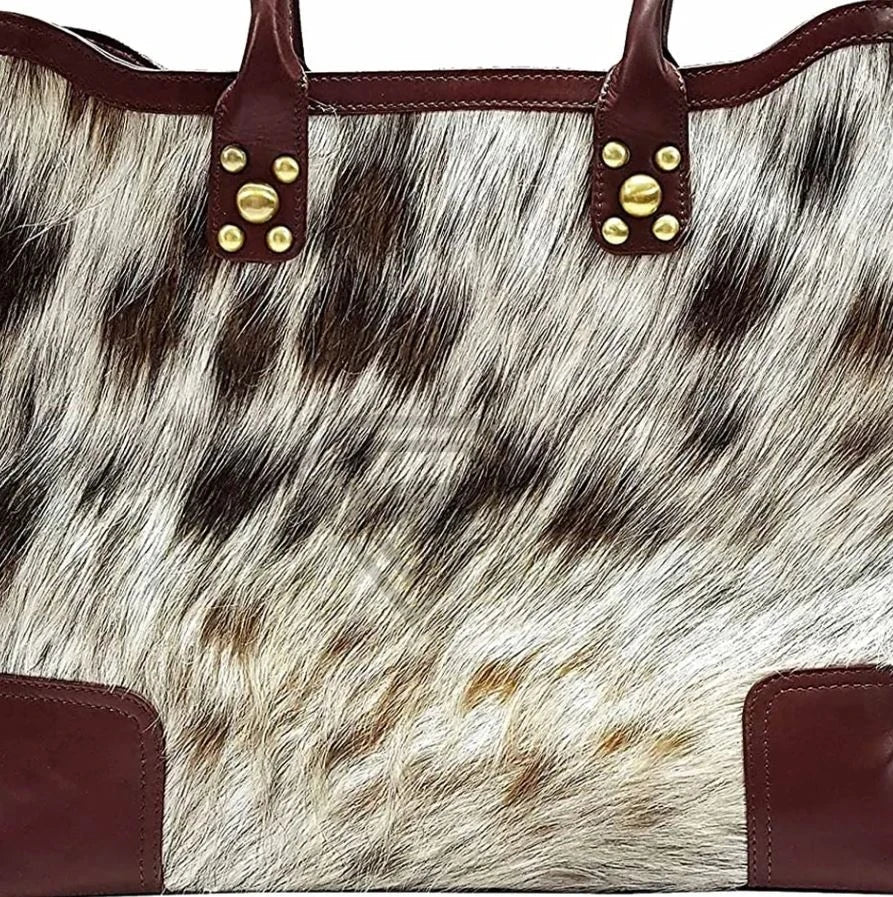 Handmade cowhide leather tote with brown leather trim, gold stud accents, and natural black and white fur pattern.