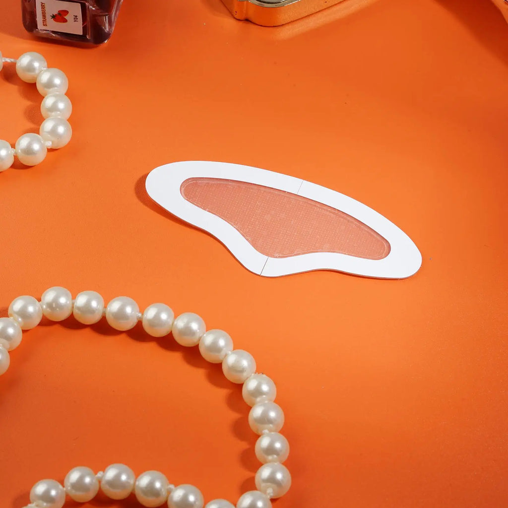 A beige, wing-shaped microneedle forehead patch on an orange background, framed by white pearl strands.