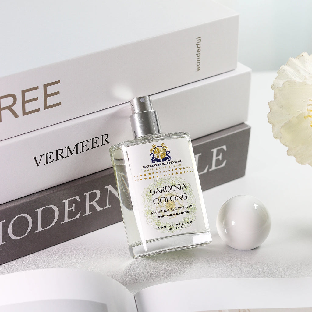 Clear glass bottle of Gardenia Oolong alcohol-free perfume with white floral label, set against books and white decor.