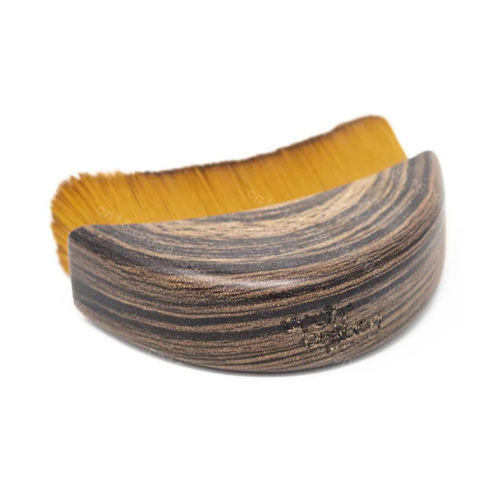 Curved facial contouring brush with a dark wood-grain handle and dense, golden-brown bristles on a white background.
