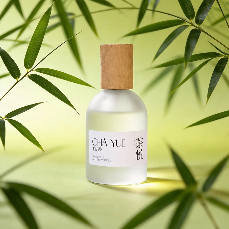 Niche white tea perfume in a frosted glass bottle with a wooden cap, set against green bamboo leaves.
