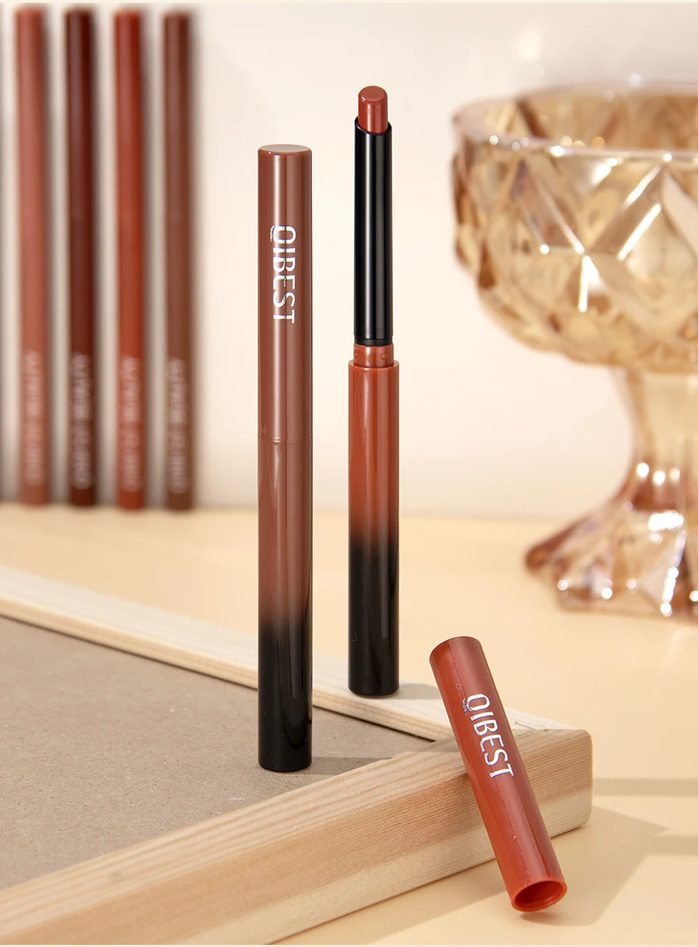QIBEST matte velvet lip liner pencil and lipstick set in warm brown ombre packaging on a wooden surface.