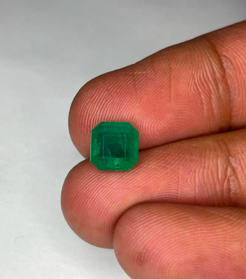 Green emerald gemstone, square octagon cut close-up held between fingers