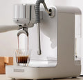 Couplux white espresso machine with chrome accents pouring a fresh shot of coffee into a crystal glass.