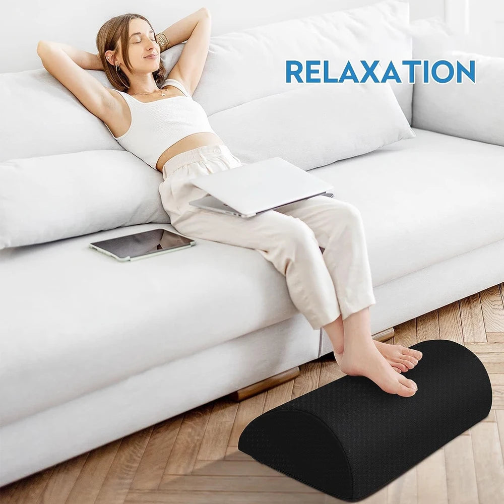 Black memory foam under desk foot rest with removable cover, used for ergonomic leg support while relaxing on sofa.