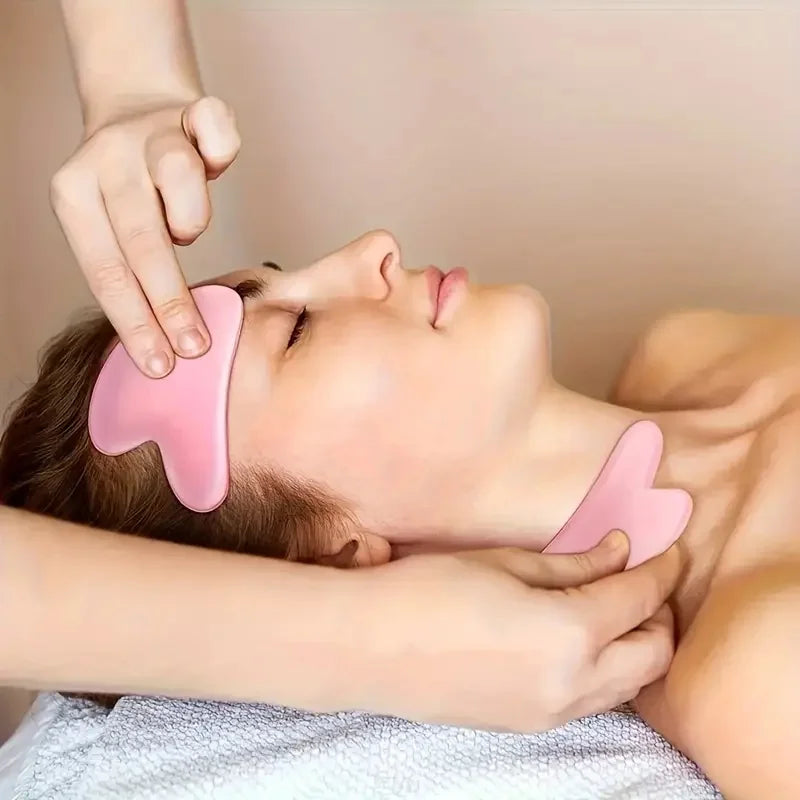 A person receiving a massage with two pink, heart-shaped, smooth stone Gua Sha facial sculpting tools.