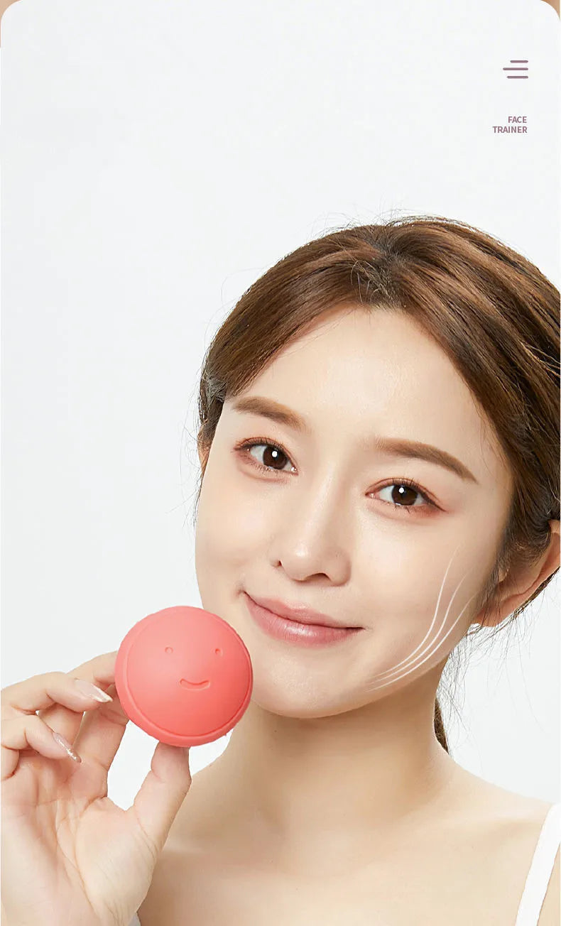 A woman holding a small, round, coral-pink silicone facial exercise tool with a smiling face embossed on it.