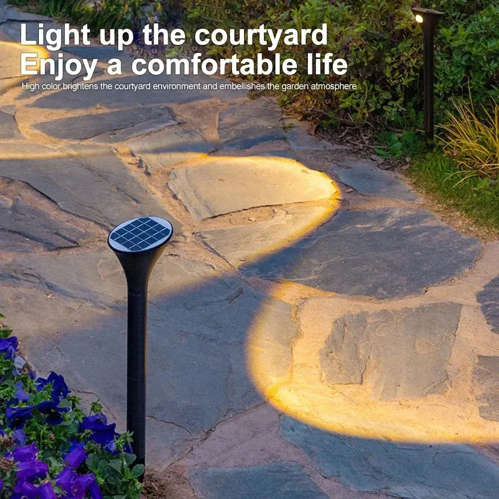 Black LED solar landscape light illuminating a stone garden walkway with warm light.