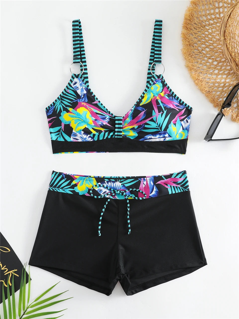 Tidesmit bikini with a tropical floral print top, striped straps, and black high-waisted shorts with a drawstring tie.