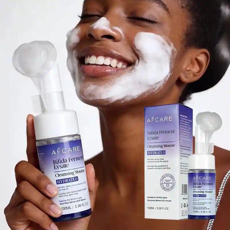Woman with face foam smiling, holding AFCARE Bifida Ferment Lysate cleansing mousse bottle with built-in brush head.