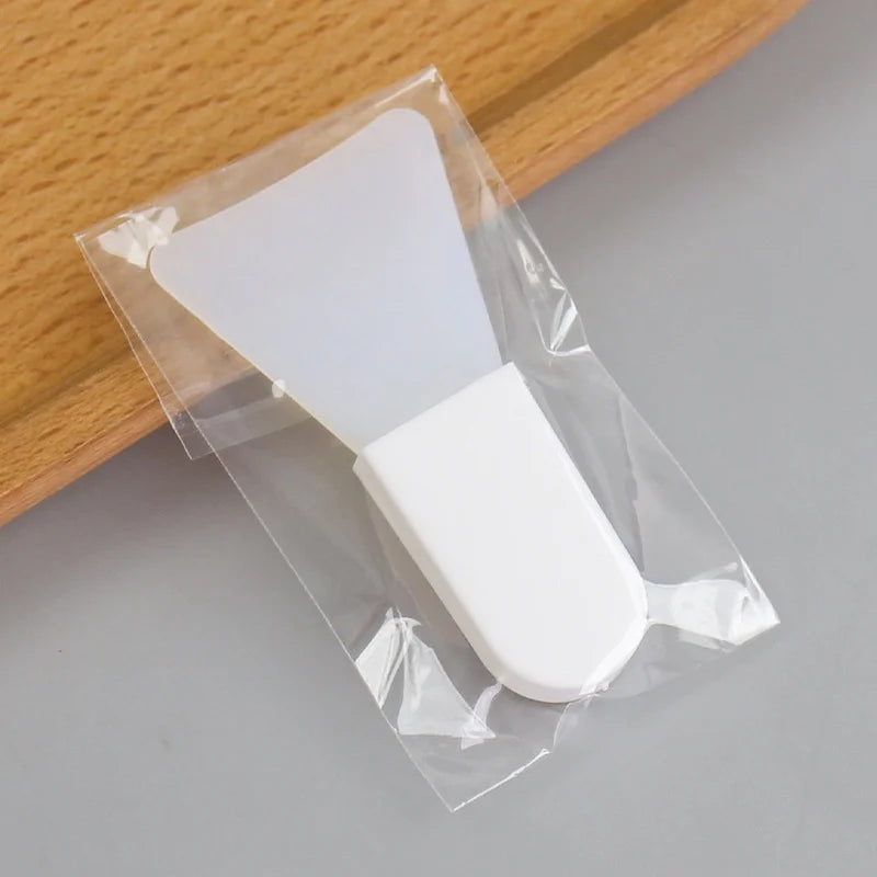 A white silicone facial mask applicator tool with a wide, flexible head in clear protective plastic packaging.
