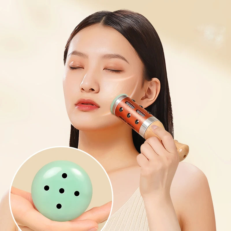 Handheld facial massage roller with copper-colored metal casing and wooden handle, used to massage skin.