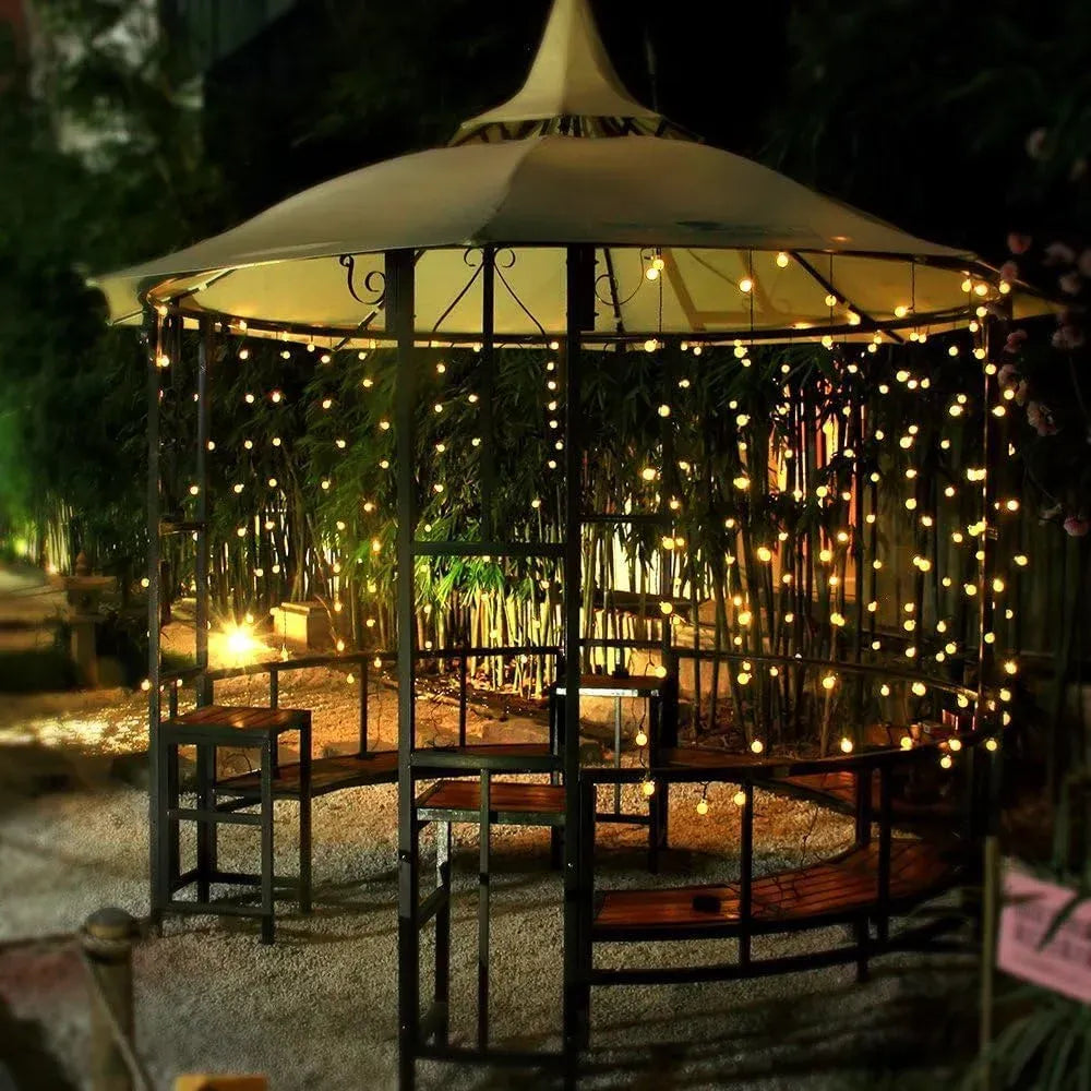 Warm LED globe string lights across a backyard gazebo frame with glowing hanging bulbs.