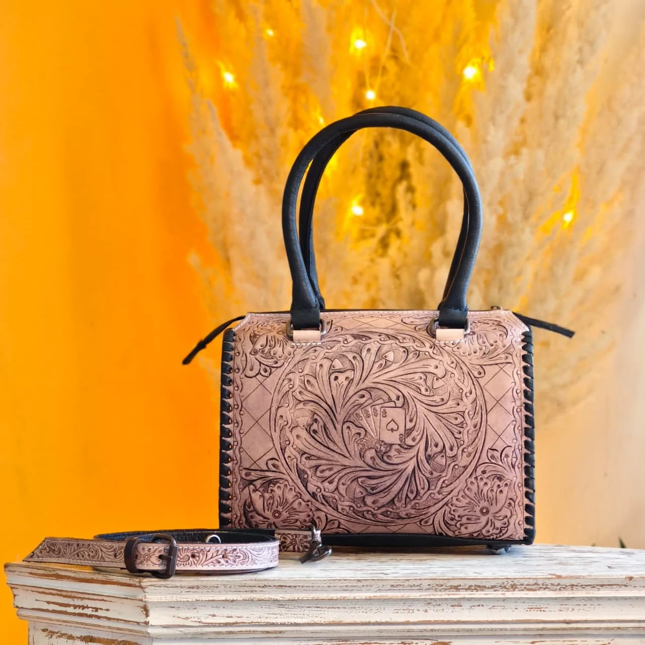 Tan hand-tooled floral leather trunk bag with black accents, featuring carved ace playing cards and a shoulder strap.