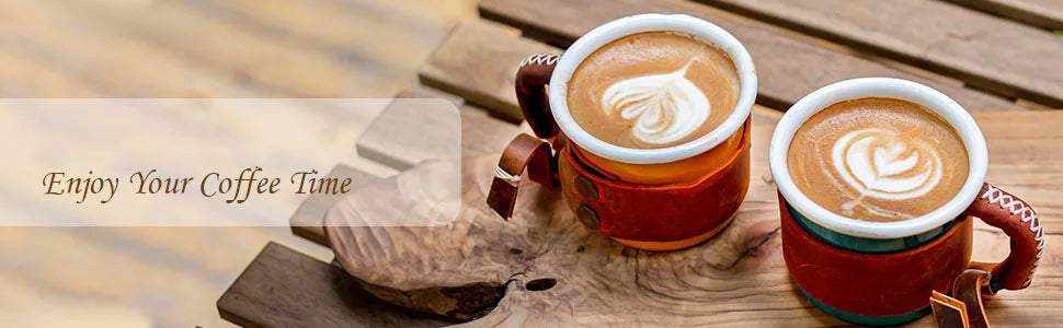 Two ceramic coffee mugs with heart latte art in stitched brown leather sleeves on a rustic wooden board.