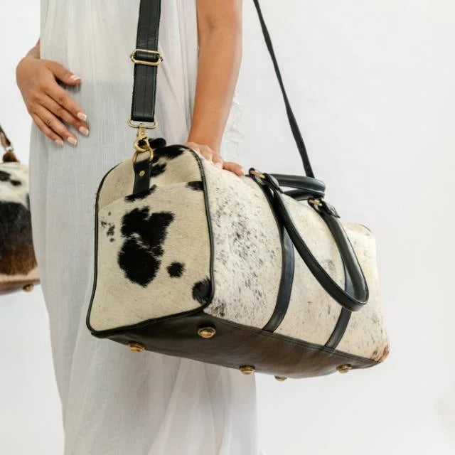 Black and white cow hide leather weekender travel duffel bag with black leather trim and shoulder strap.