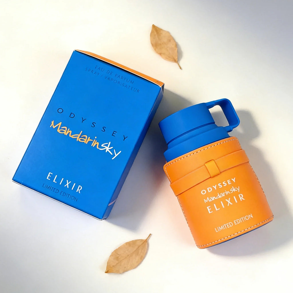 Odyssey Mandarin Sky Elixir perfume in a blue box and a cylindrical bottle with an orange leather-like sleeve.