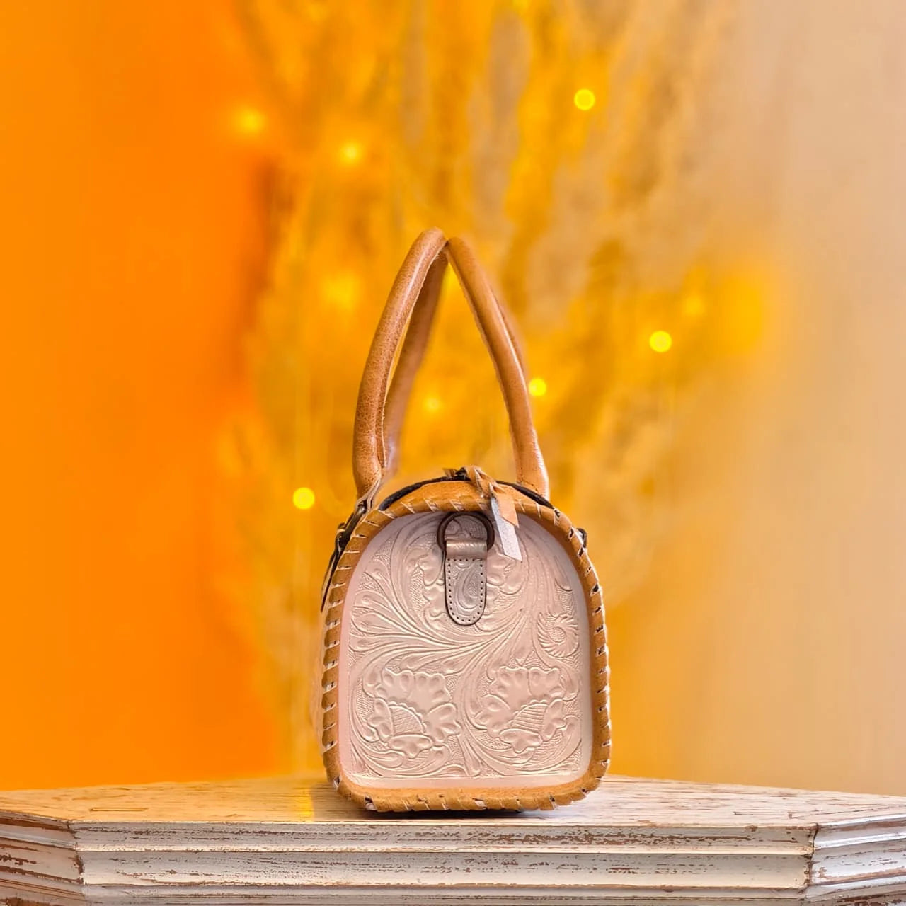 Tan genuine leather mini speedy duffel bag with hand-tooled floral carvings and whipstitch trim. Designer handbag.