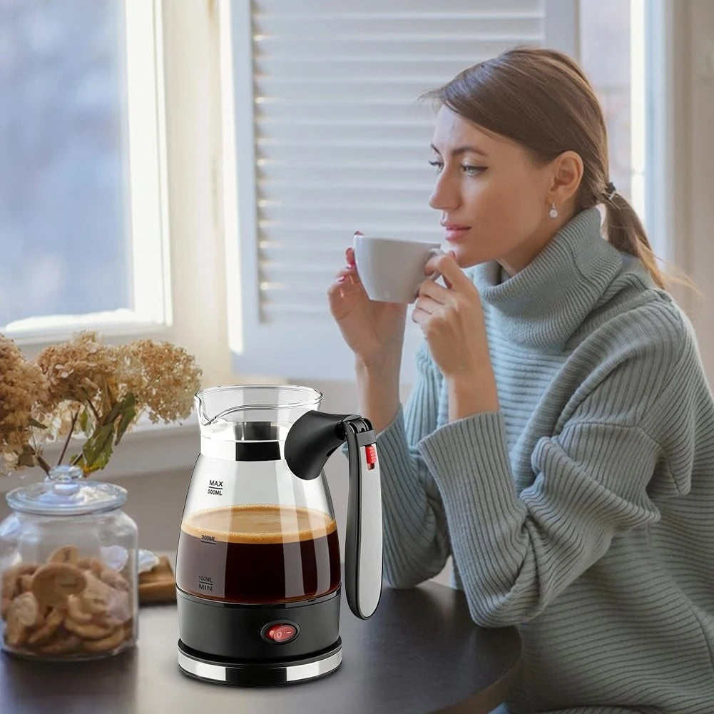 Compact black and glass electric coffee maker with 500ml capacity on a table next to a woman drinking coffee.