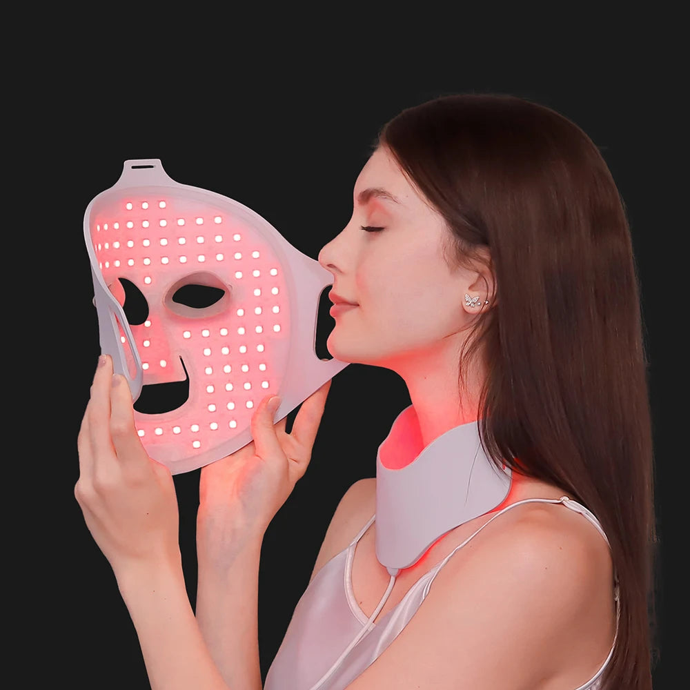 Woman holding a flexible white silicone LED face mask emitting red light, with a matching LED neck piece attached.