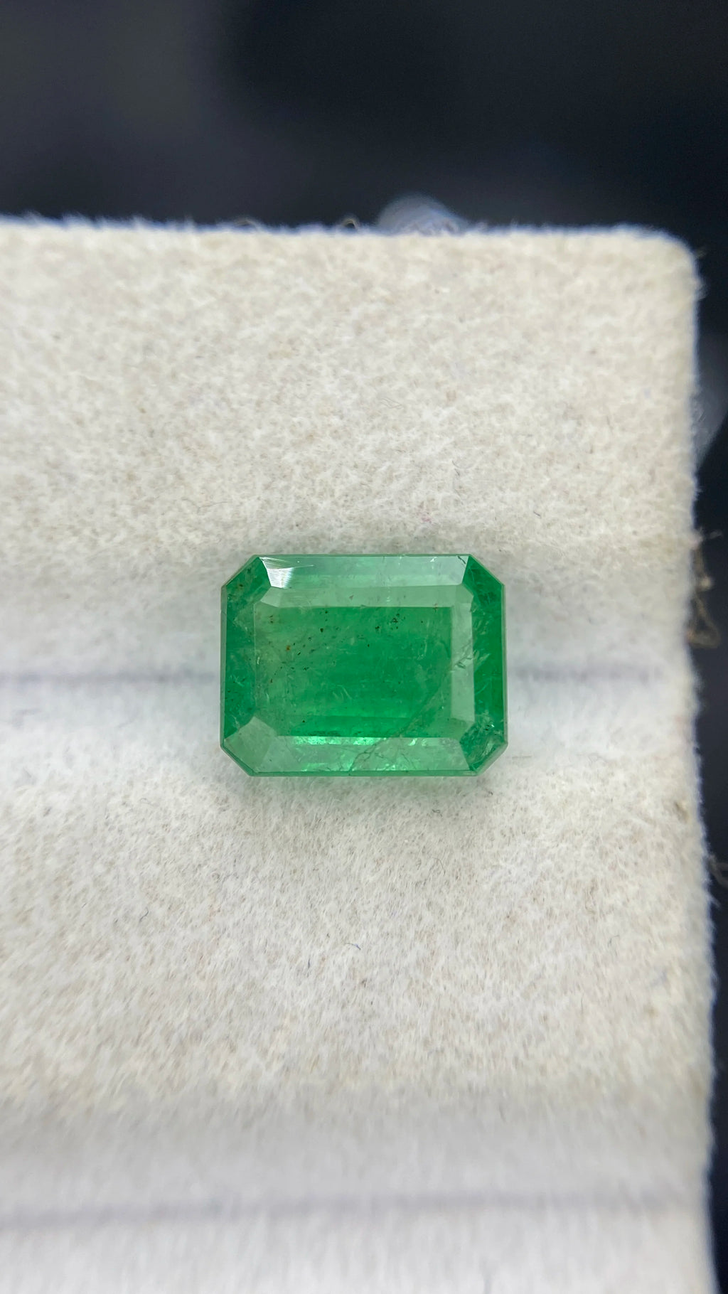 Green octagon emerald-cut loose gemstone centered on white felt