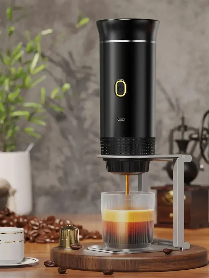Black portable capsule coffee maker with USB-C charging on a silver stand, pouring espresso into a glass cup.