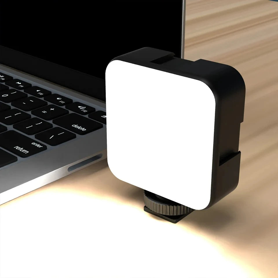 Small square LED video light with a black frame and white diffuser, attached to a laptop for extra lighting.